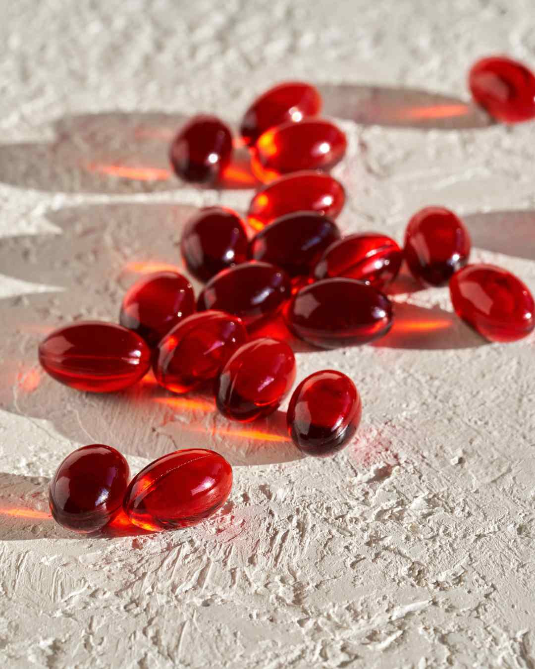 Več temno rdečih kapsul astaksantina na hrapavi svetli podlagi – prikaz naravne podpore za sklepe, mišice in zmanjšanje vnetij z močnim antioksidativnim učinkom.